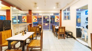 L’intérieur d’un restaurant avec des tables et des chaises en bois, un comptoir où sont exposés des plats, et une vue sur la rue.