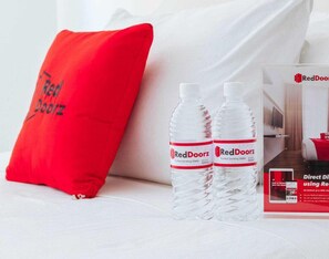 A hotel room with a red pillow, two RedDoorz water bottles, and a RedDoorz brochure.