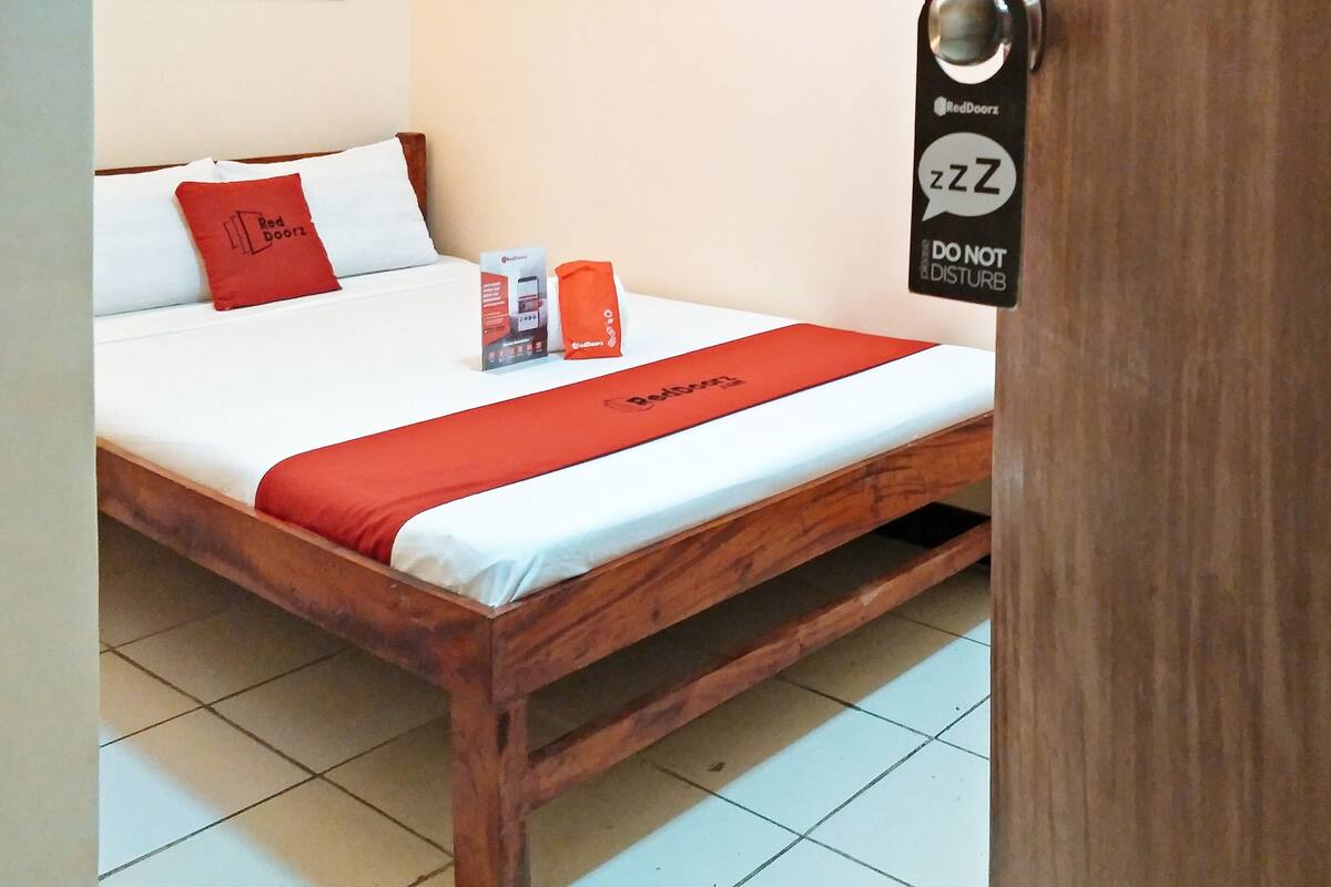 Ein hölzernes Bett mit einer weißen und roten Bettdecke, einem roten Kopfkissen und einem RedDoorz-Schild an der Tür.