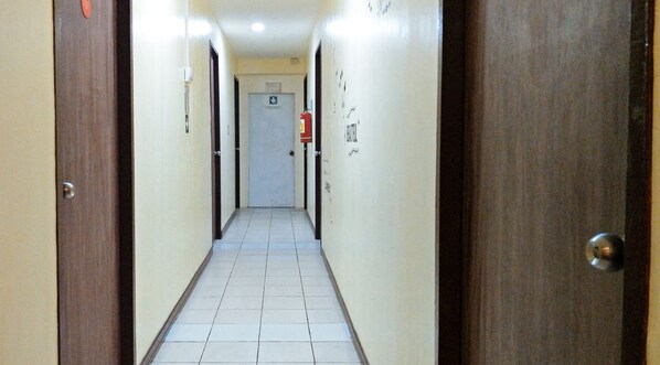 A narrow hallway with doors on both sides, a tiled floor, and a fire extinguisher mounted on the wall.