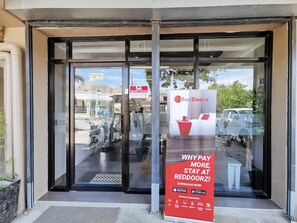 L’entrée d’un hôtel, avec une porte en verre, un avis de sécurité et une publicité pour RedDoorz.