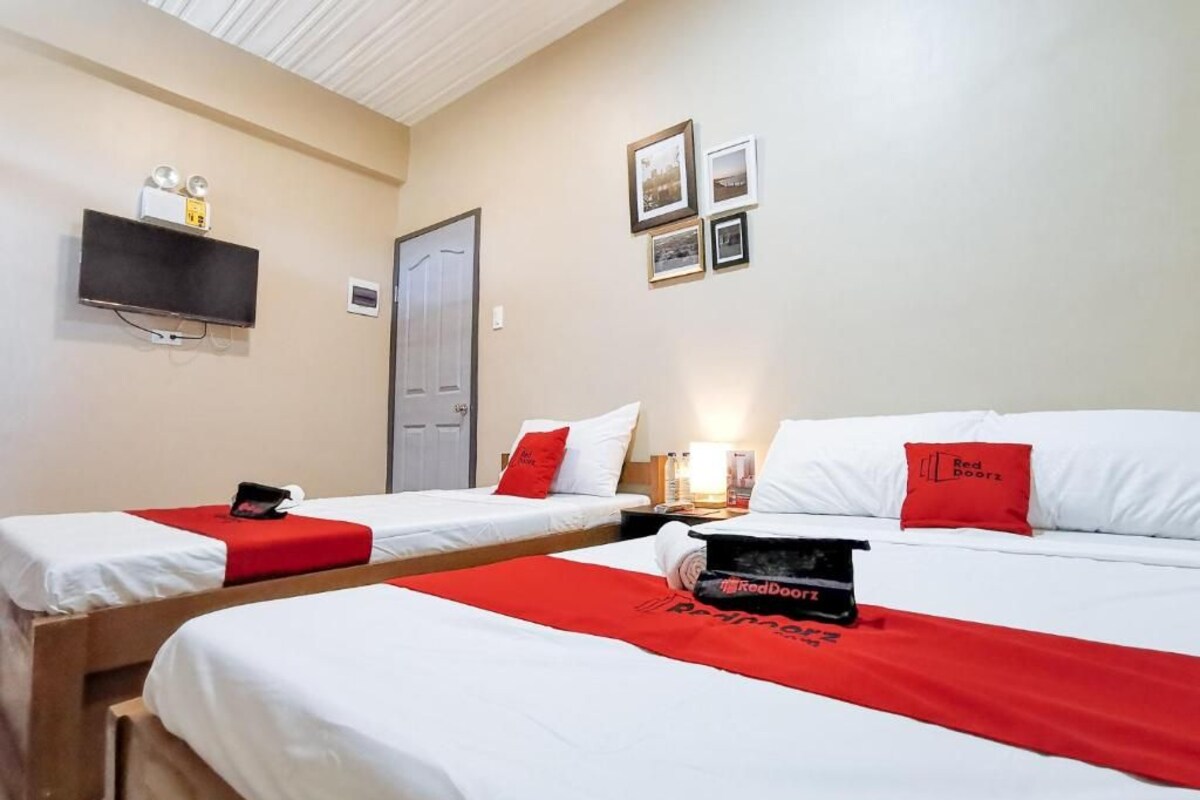 Ein Hotelzimmer mit zwei Betten, jedes mit einer rot-weißen Tagesdecke, einem an der Wand montierten Fernseher und gerahmten Bildern.