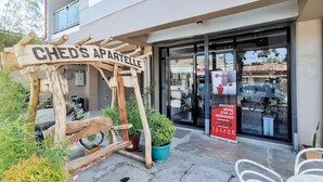 Un letrero de madera con la inscripción "CHED'S APARTELLE" frente a un edificio con puerta de vidrio, plantas en macetas y un anuncio de RedDoerz.