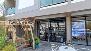 Un edificio con un letrero que dice "CHED'S APARTELLE" y una entrada con puerta de vidrio. Hay mesas y sillas al aire libre al frente.