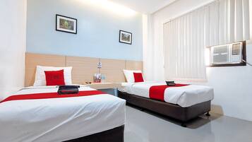 A hotel room with two beds, each with a red and white bedspread, a wooden headboard, and a small table with a red pillow and a Red Doorz bag.