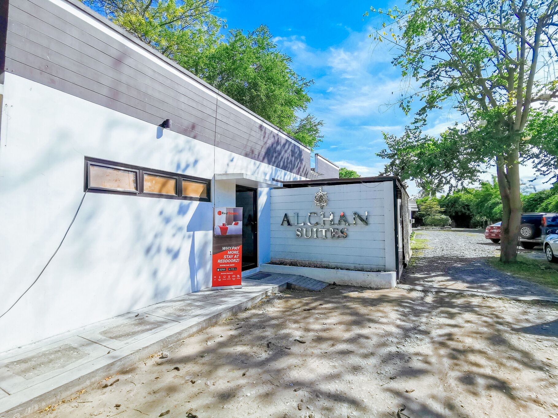 The exterior of Alchan Suites, featuring a white building with a large signboard displaying the name and a logo.