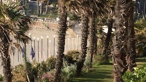 Ein angelegter Garten mit Palmen, einer Rasenfläche und einem Gebäude im Hintergrund, das mit Flaggen geschmückt ist.