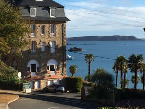 A stone building with arched windows and a balcony, overlooking a coastal area with palm trees and a clear view of the sea. - Quiet, bright, renovated apartment, 50 meters from the beach at TRESTRAOU PERROS GUIREC (Perros-Guirec)