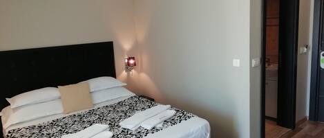 A neatly made bed with white and black patterned bedding, a black headboard, and a wall-mounted light fixture.