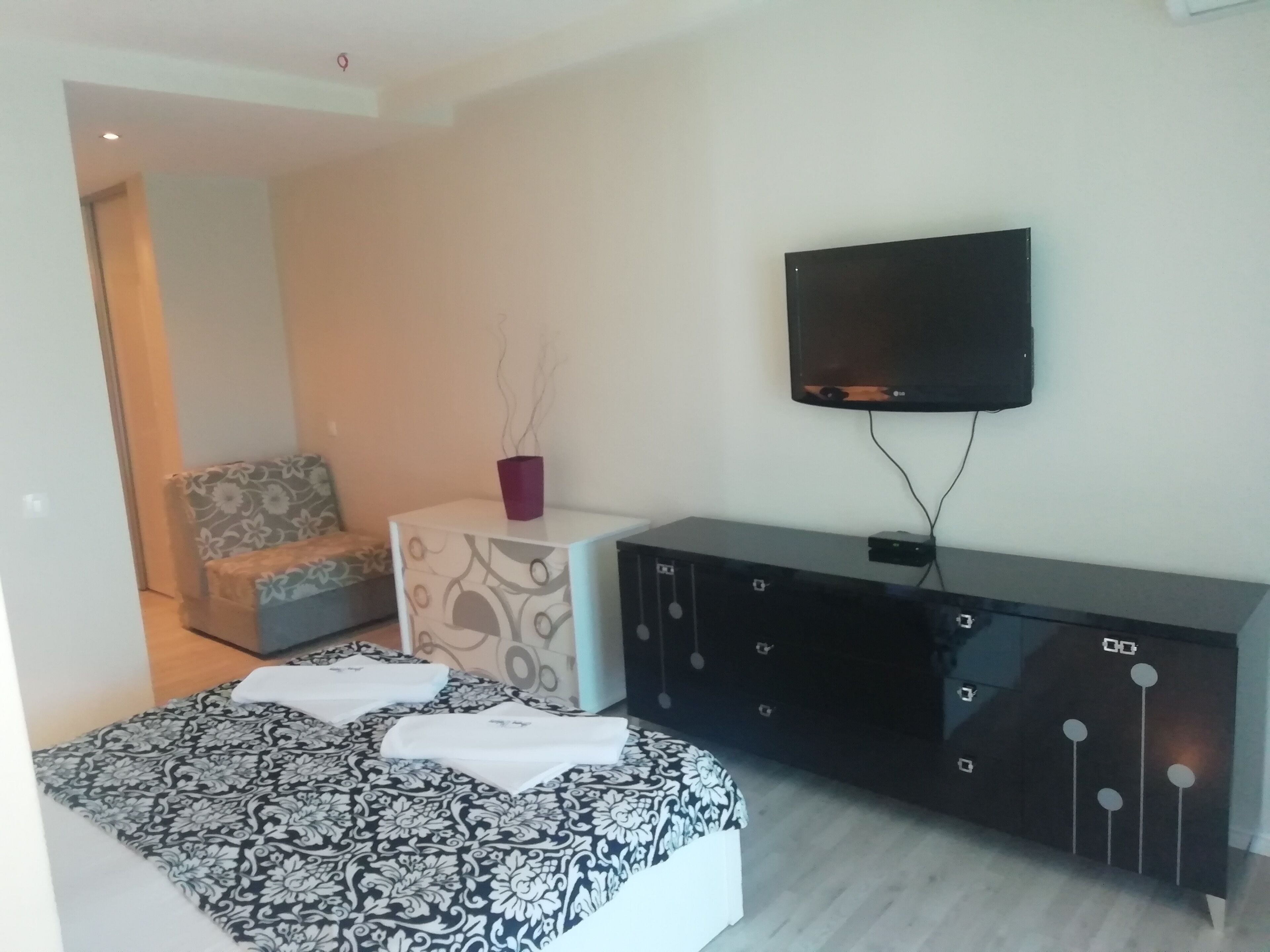 Un dormitorio moderno con una cama, un pequeño sofá, un televisor y un armario.