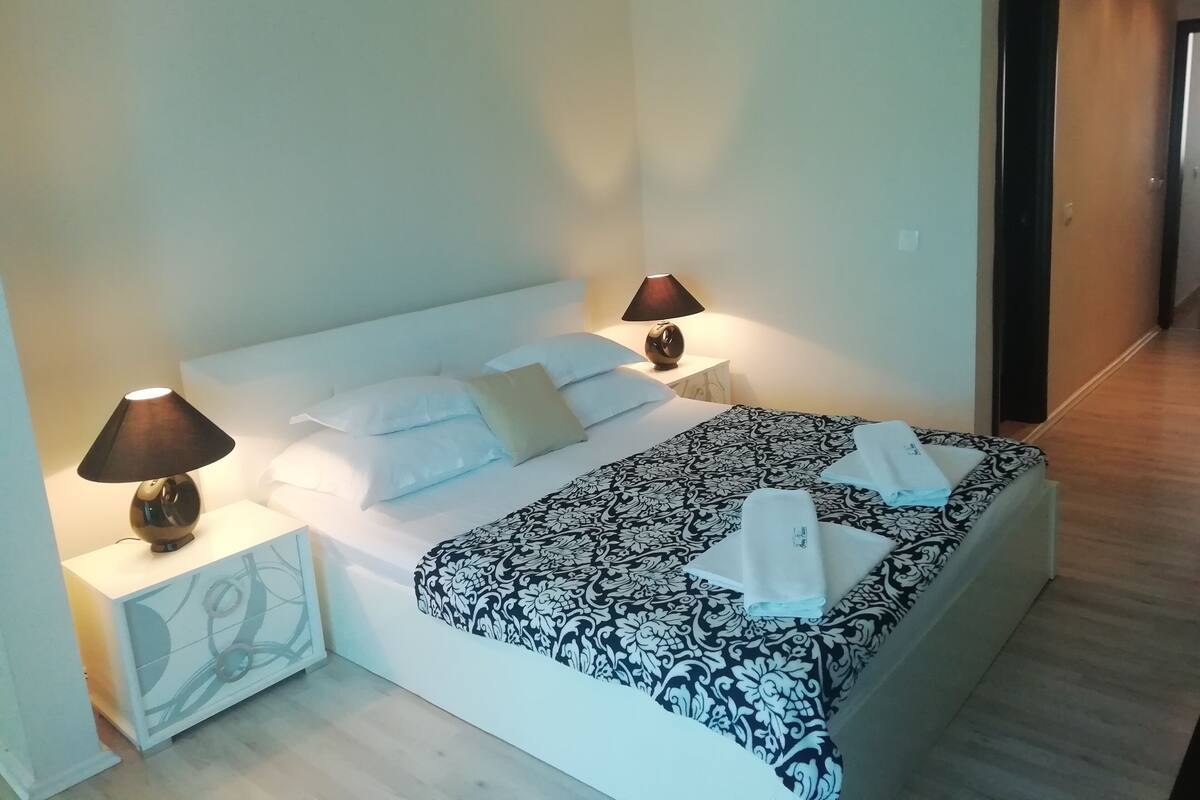 Una cama bien hecha con una colcha estampada, dos lámparas de noche y una mesita de noche blanca con un diseño decorativo.