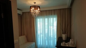 Un salon avec un canapé beige, un lustre et une grande fenêtre ornée de rideaux légers.