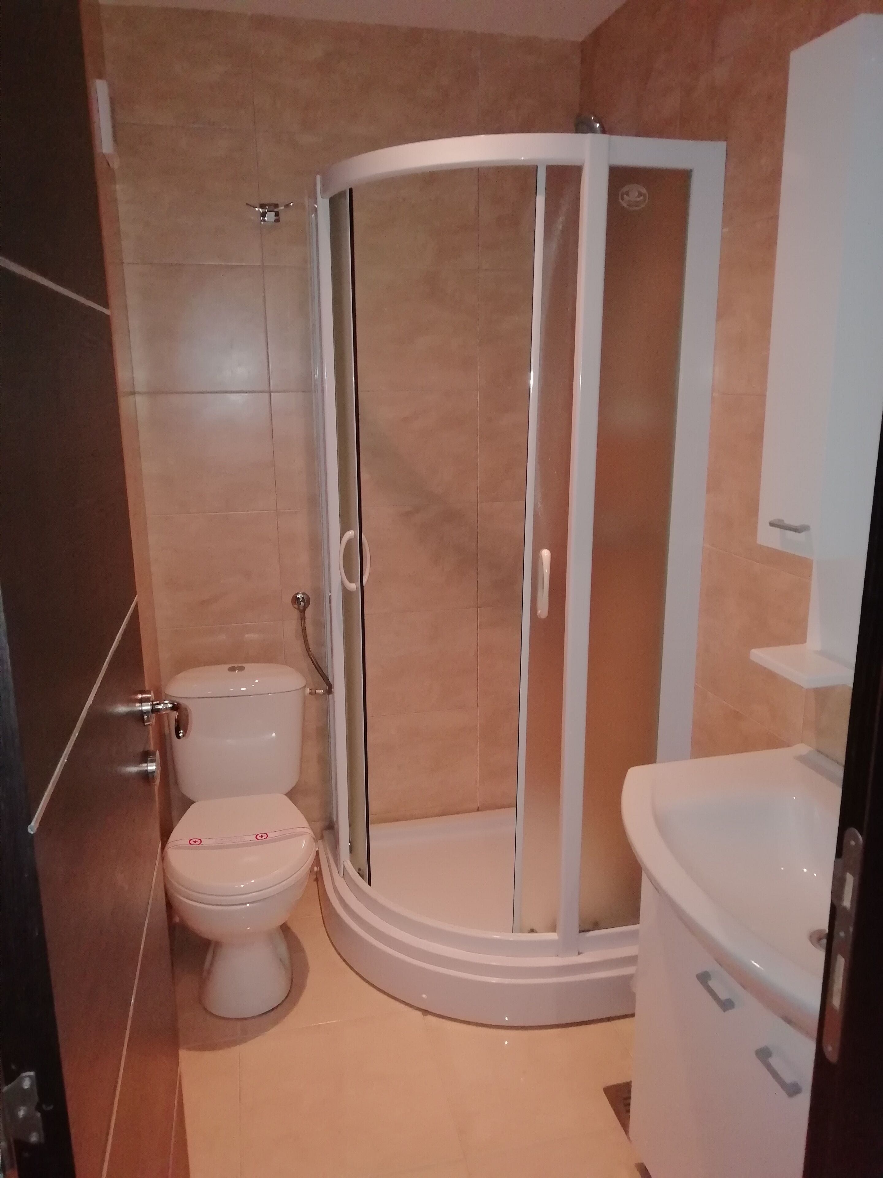 A bathroom with a glass-enclosed shower, a toilet, and a sink.