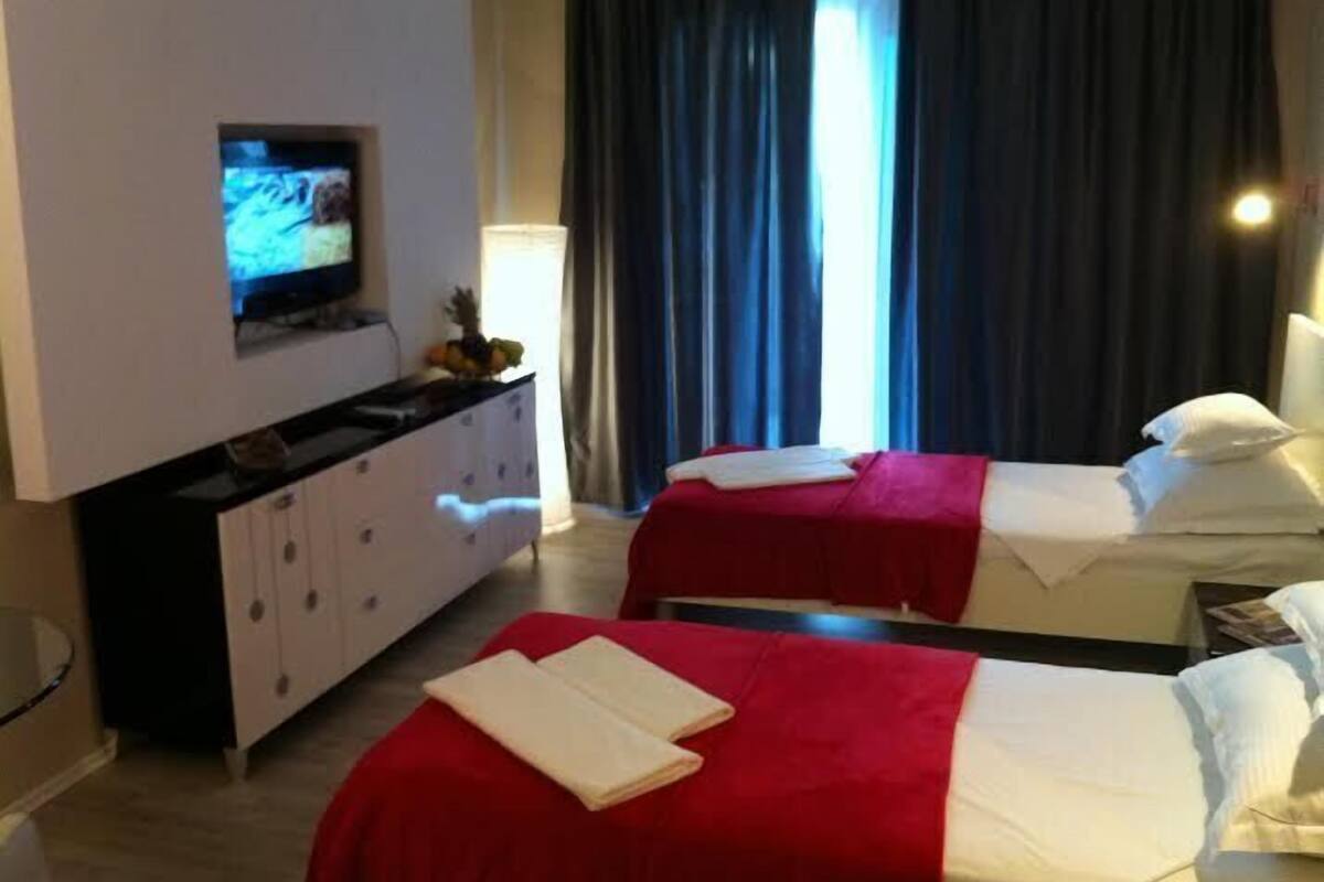 Habitación de hotel con dos camas, televisión, cómoda y ventana con cortinas.
