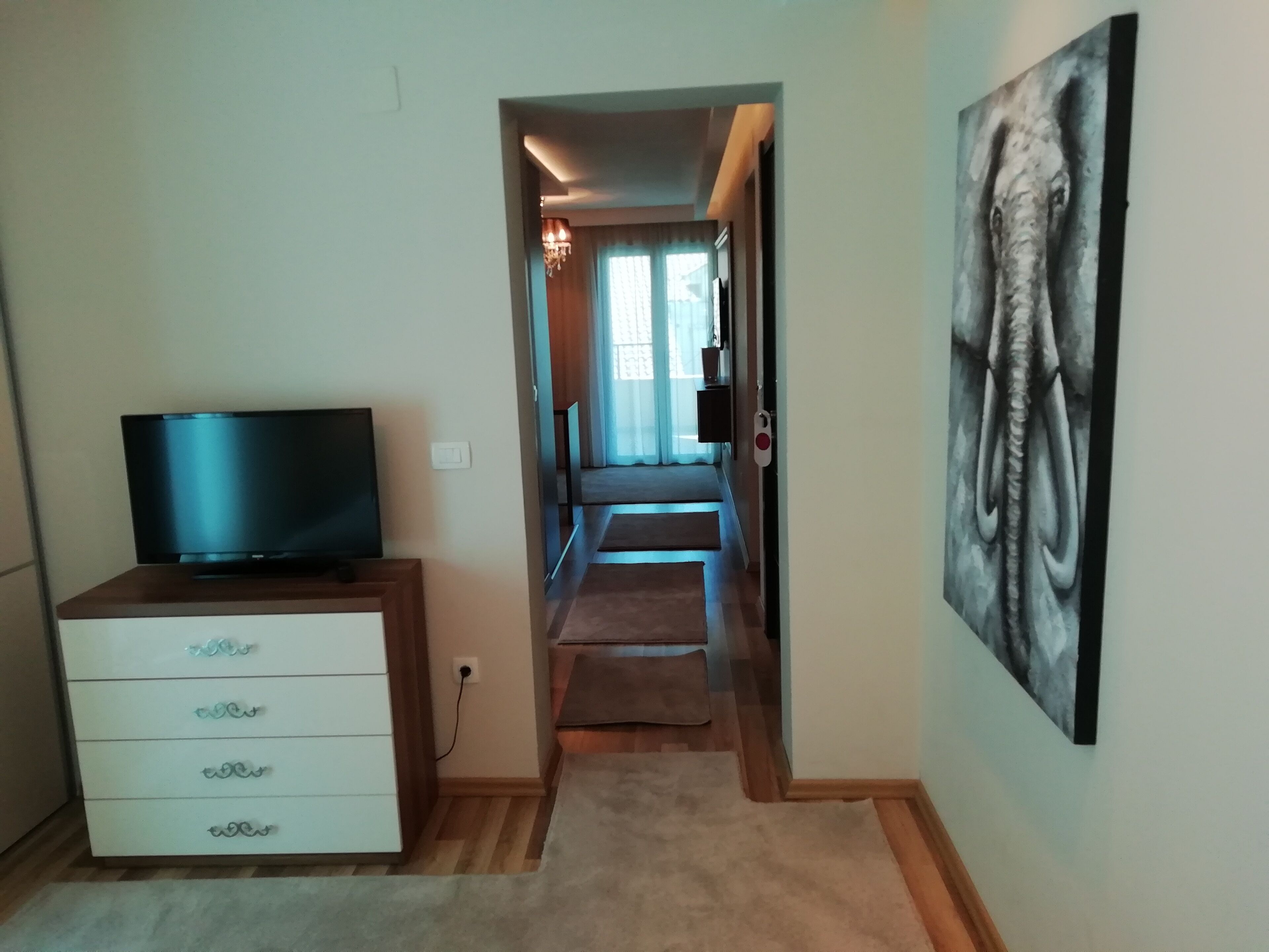 Un pasillo con un televisor sobre un mueble de madera, un aparador blanco, un cuadro en la pared y piso alfombrado.