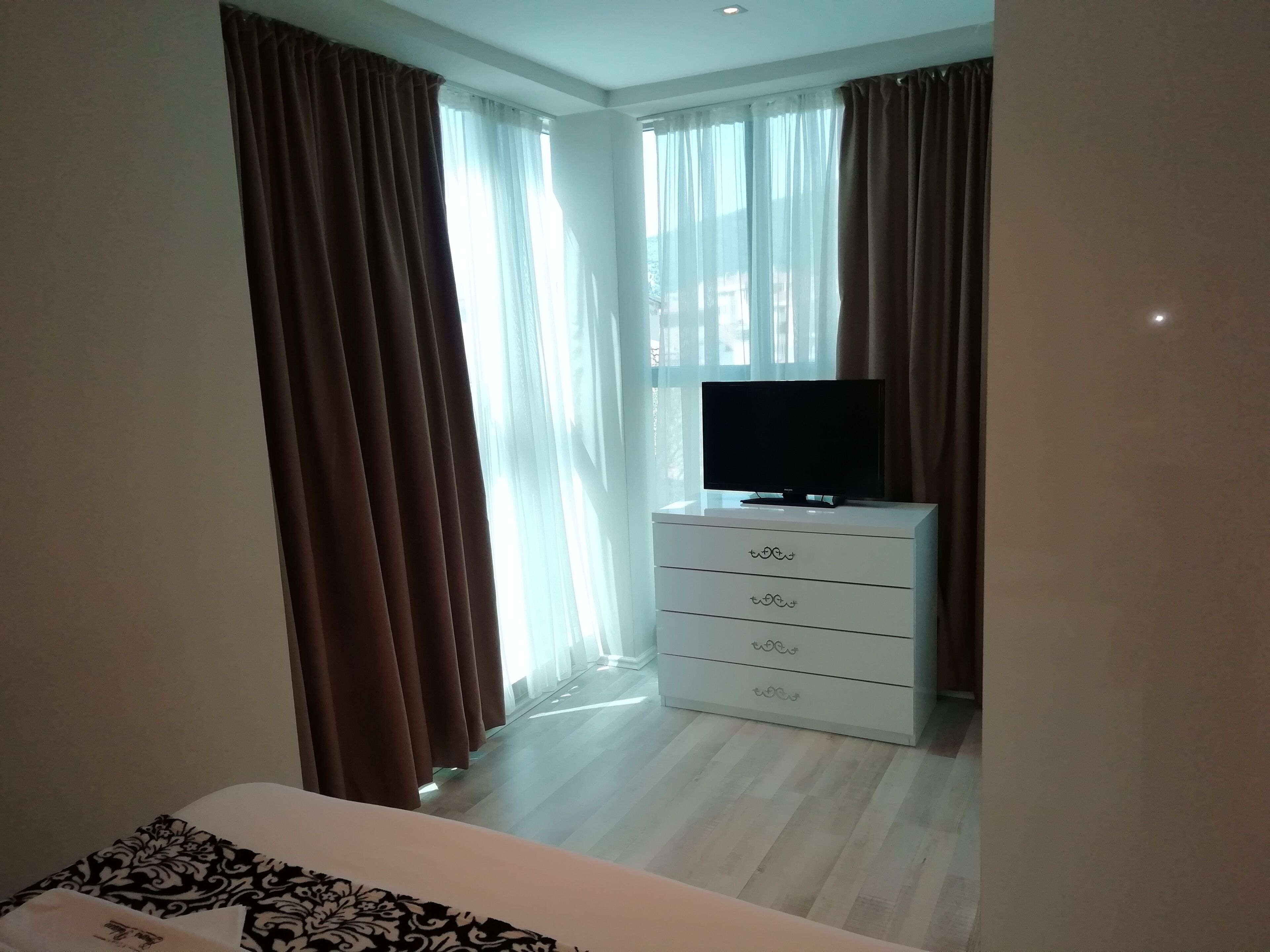 Hotellihuone, jossa on sänky, televisio lipaston päällä ja verhot ikkunoissa.