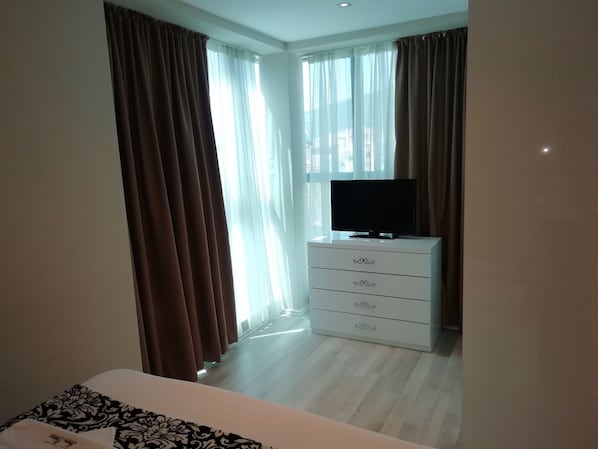 Una habitación de hotel con una cama, un televisor en una cómoda y cortinas en las ventanas.