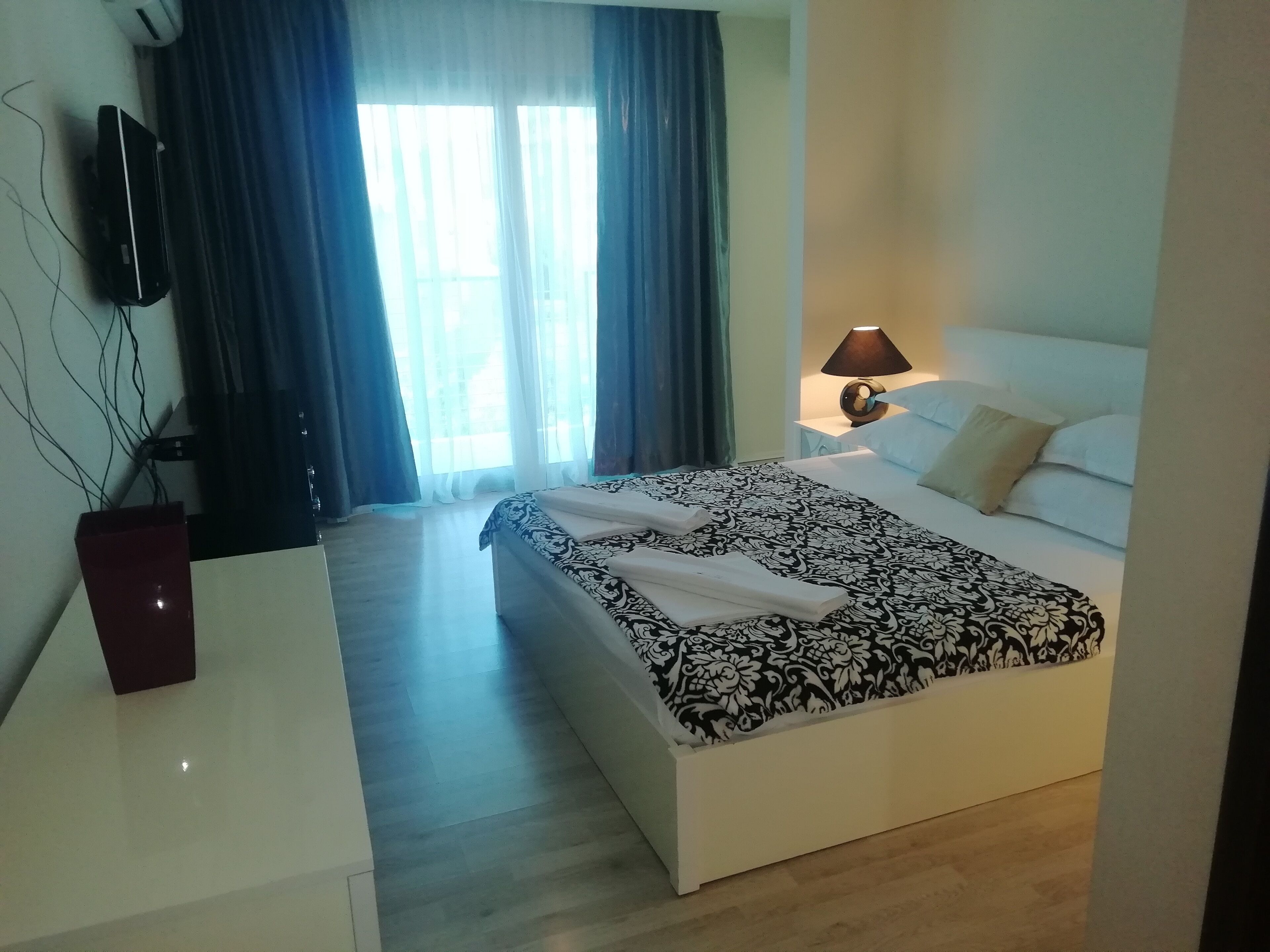 Camera d'albergo con un letto, una lampada da comodino, una TV a parete e una finestra con tende.