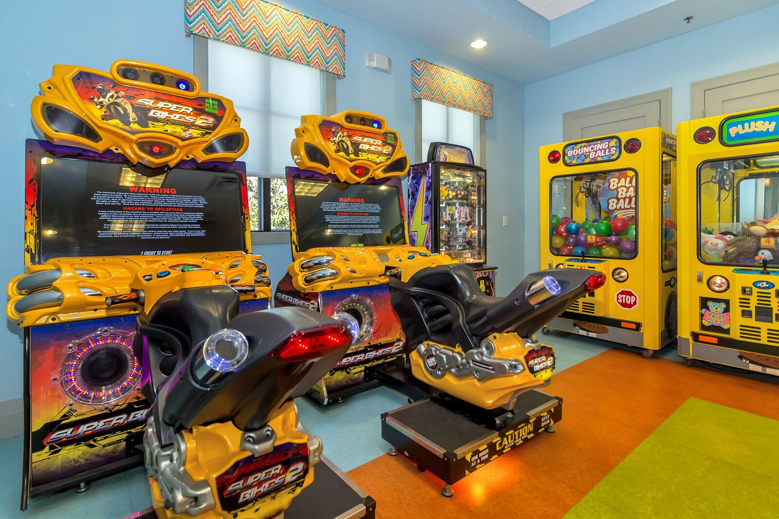 Arcade machines and a bus-shaped game in a brightly lit room with blue walls and a green carpet.