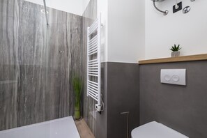 Un baño moderno con pared de mármol, un toallero blanco, una pequeña planta en maceta y un aplique de pared.