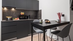 A modern kitchen with dark cabinetry, a black countertop, and a dining area with two chairs. - Deluxe Apartments & Rooms In the Center (Rijeka)