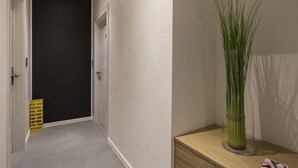 A hallway with a black door, a wooden bench, and a clear vase with green plants. - Deluxe Apartments & Rooms In the Center (Rijeka)