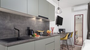A modern kitchen with grey cabinets, a black countertop, and a built-in stove. There are bar stools and a bed visible in the background. - Deluxe Apartments & Rooms In the Center (Rijeka)