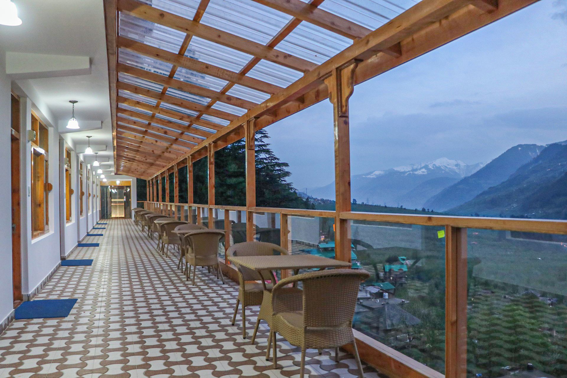 A corridor with a patterned floor leading to a balcony with wicker furniture and a view of mountains.