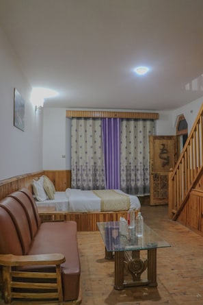 A room with a wooden sofa, a glass coffee table, a bed with patterned curtains, and a wooden staircase.