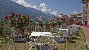 A terrace with metal chairs and tables, a flower garden, and a mountain backdrop.