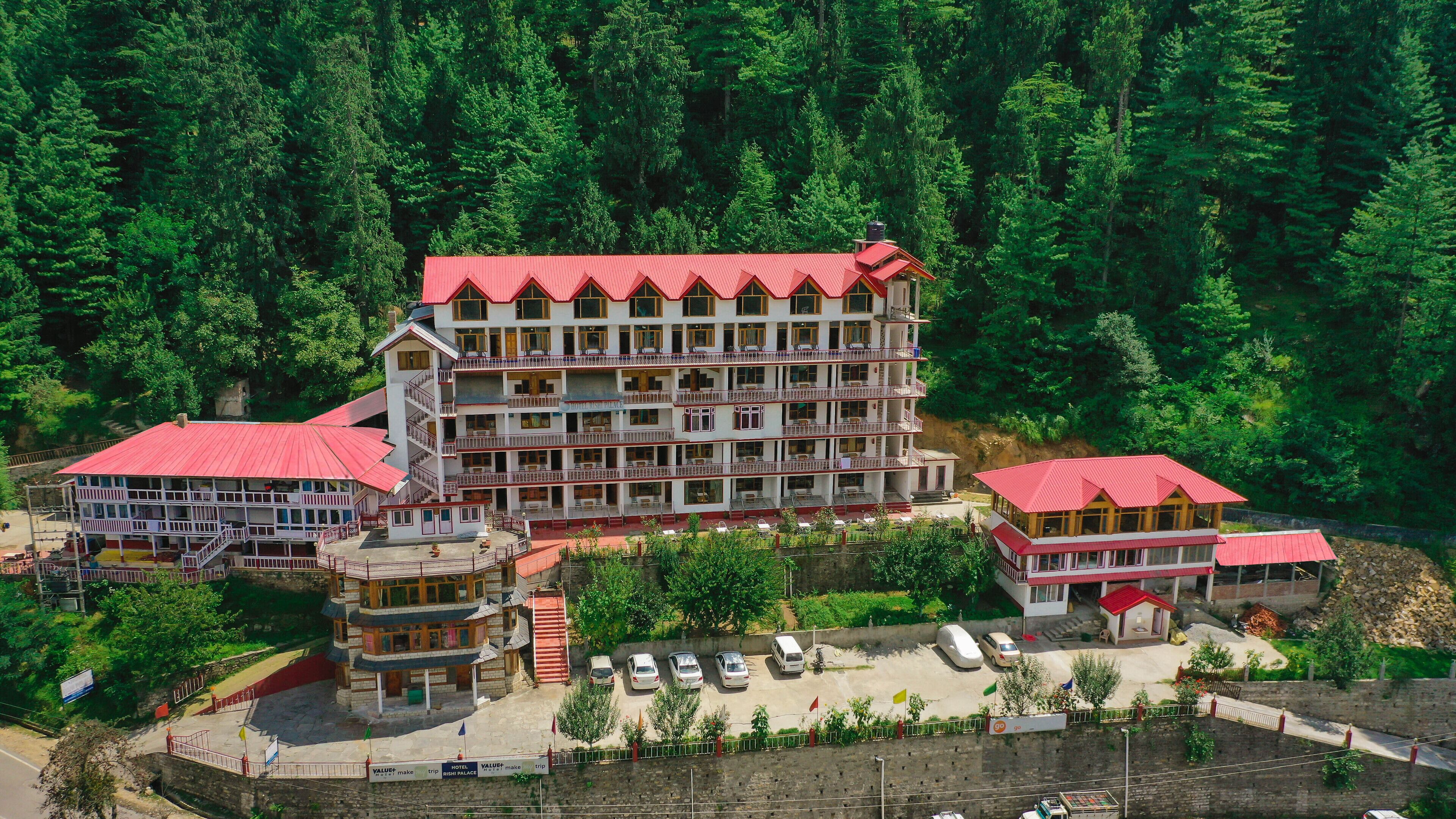 A multi-story hotel with a red roof, surrounded by dense forest.
