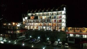 A multi-story hotel with several balconies and a parking area with cars.