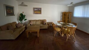Uma sala de estar com um sofá, uma mesa de centro, uma mesa de jantar com cadeiras, um vaso de planta e obras de arte nas paredes.