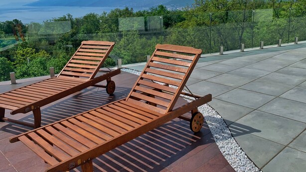 Two wooden lounge chairs on a tiled patio with a view of mountains and a body of water. - Villa Flora Apartment (Kastav)