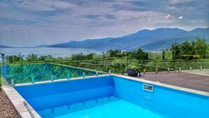 A swimming pool with clear blue water, surrounded by a glass railing, and a view of mountains and a body of water in the background. - Villa Flora Apartment (Kastav)