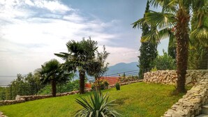 A landscaped garden with a stone wall, palm trees, and a view of distant mountains. - Villa Flora Apartment (Kastav)