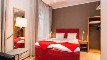 A modern hotel room with a large bed, a bedside table, a mirror, and a wardrobe.