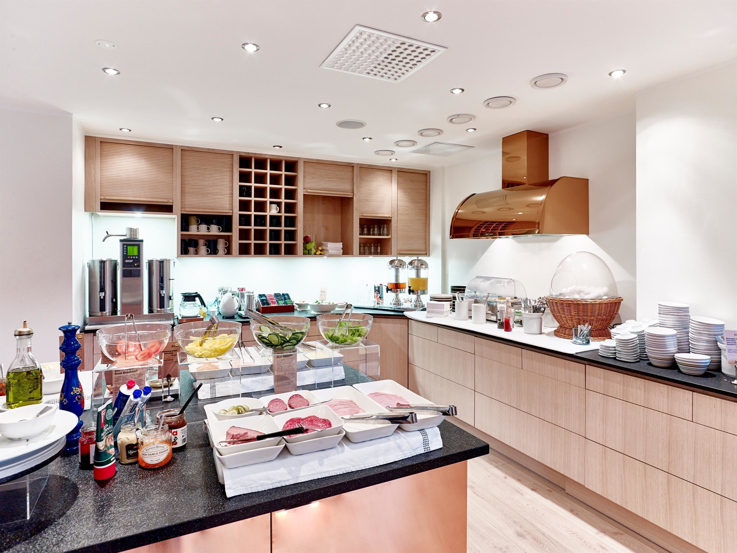 A modern breakfast buffet with a variety of food items and beverages, stainless steel appliances, and wooden cabinetry.