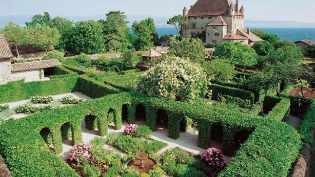 Un edificio histórico con una torre, rodeado de jardines cuidados y senderos.