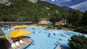 Una gran piscina al aire libre con varias secciones, rodeada de exuberante vegetación y montañas al fondo.