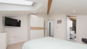 Un dormitorio con una cama, un televisor montado en la pared y un tragaluz.