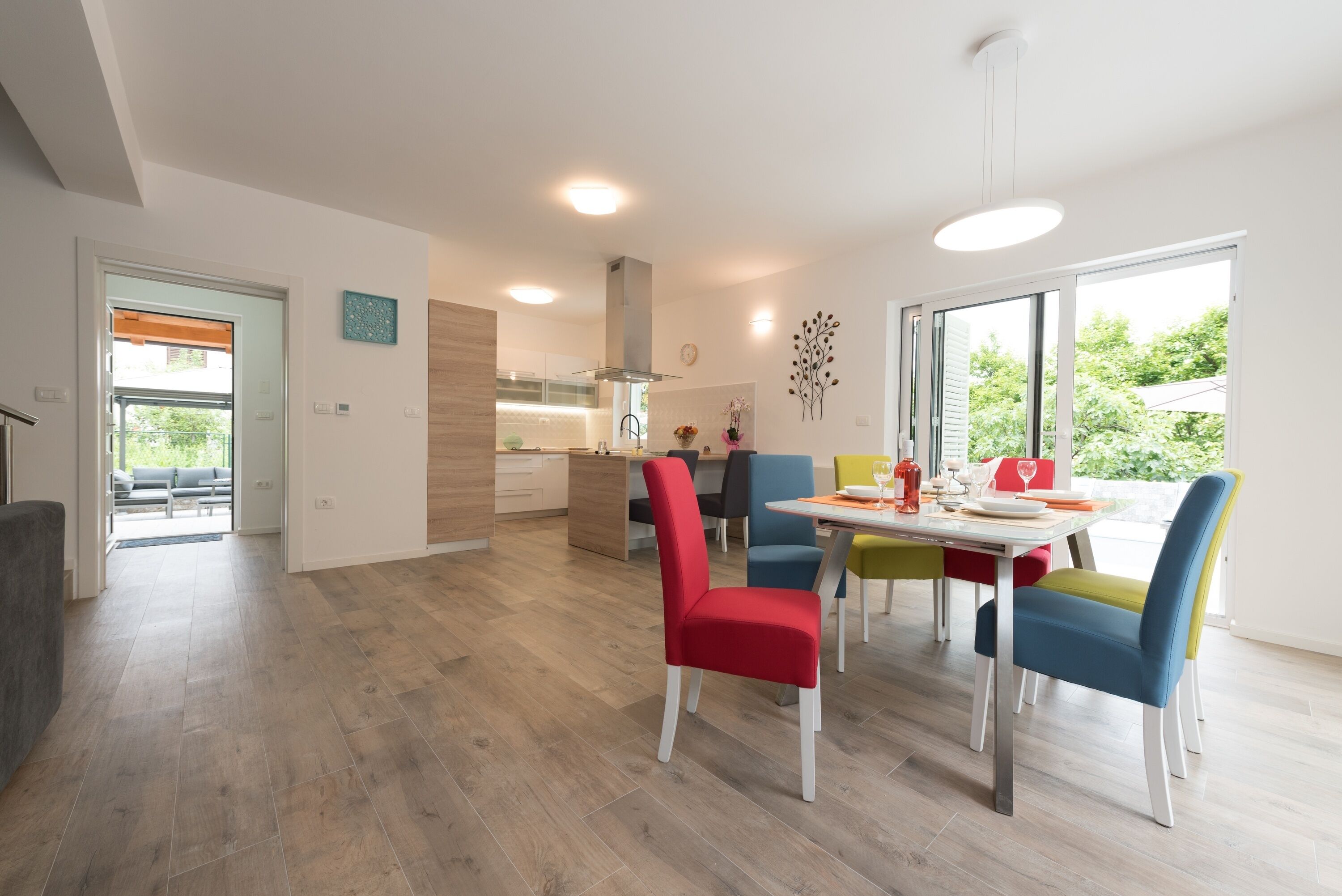 Een moderne eetruimte met een houten vloer, een wit plafond en een eettafel met kleurrijke stoelen.