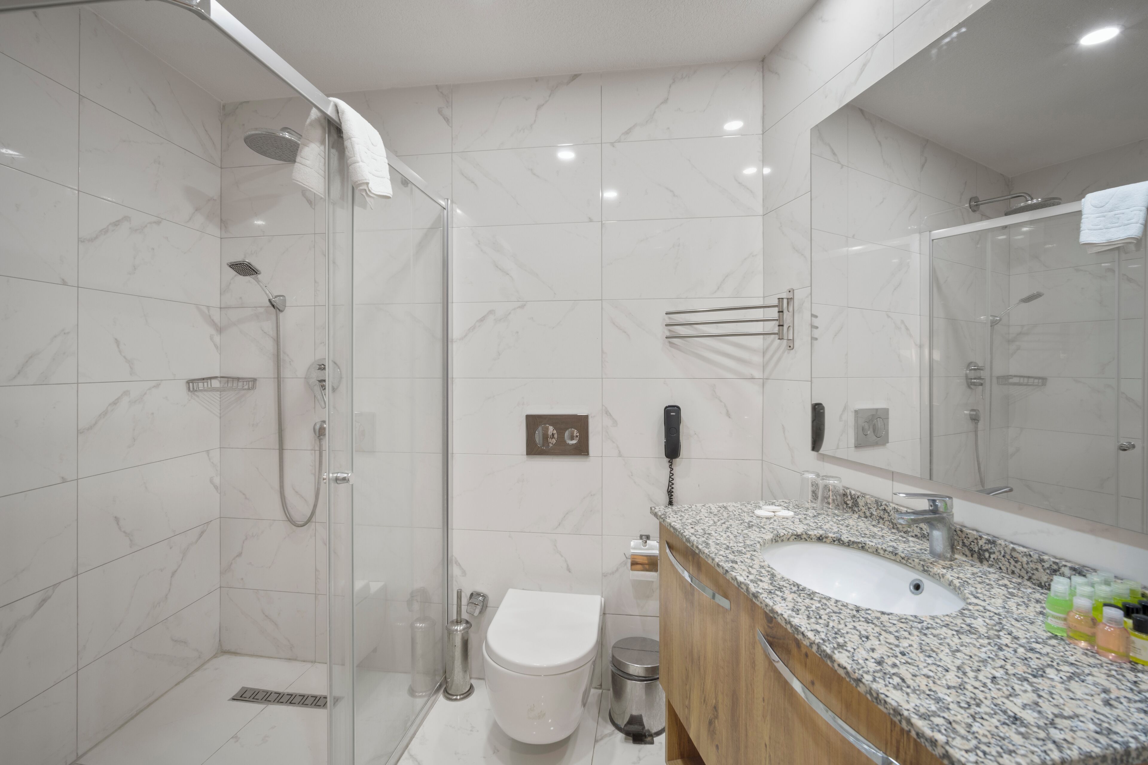 A modern bathroom with a glass-enclosed shower, a white toilet, a granite countertop sink, and a large mirror.