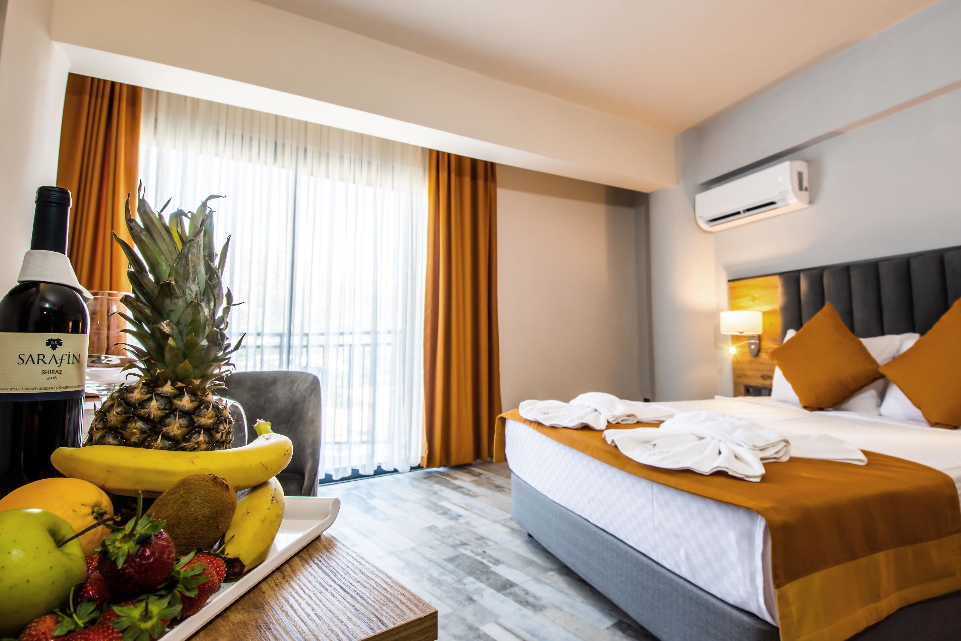 A hotel room with a bed, a table with fruit and a bottle, and a window with curtains.