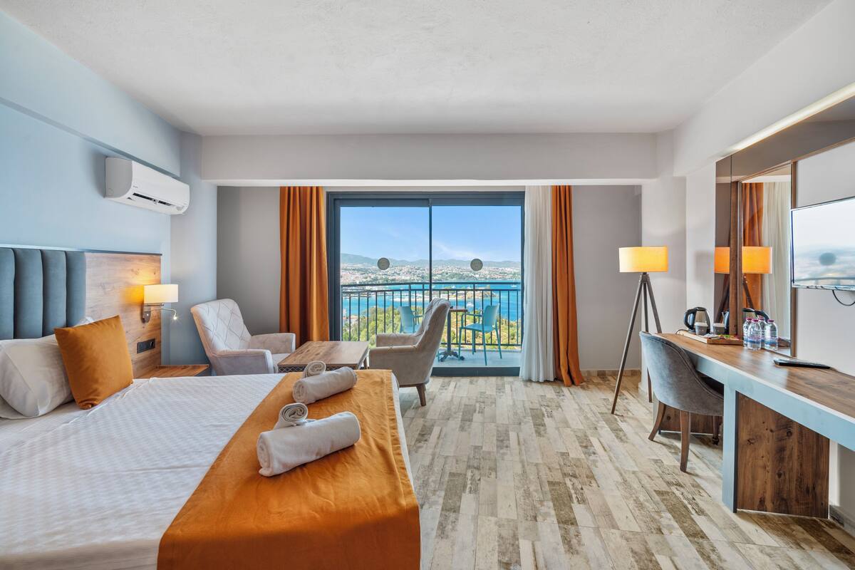 Quarto de hotel com cama, escrivaninha, cadeiras e varanda com vista.