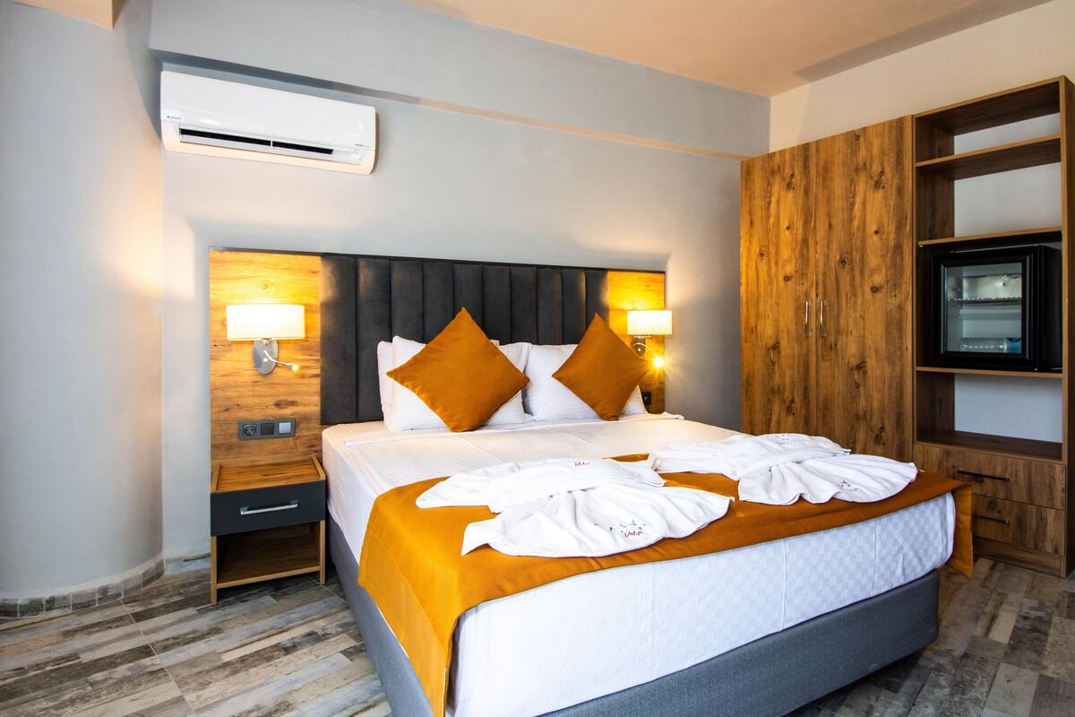 Quarto de hotel com uma cama grande, duas mesas de cabeceira com luminárias, um guarda-roupa de madeira e uma televisão.