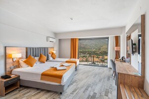 Habitación de hotel con dos camas, un escritorio, una silla, un balcón con mesa y un televisor.