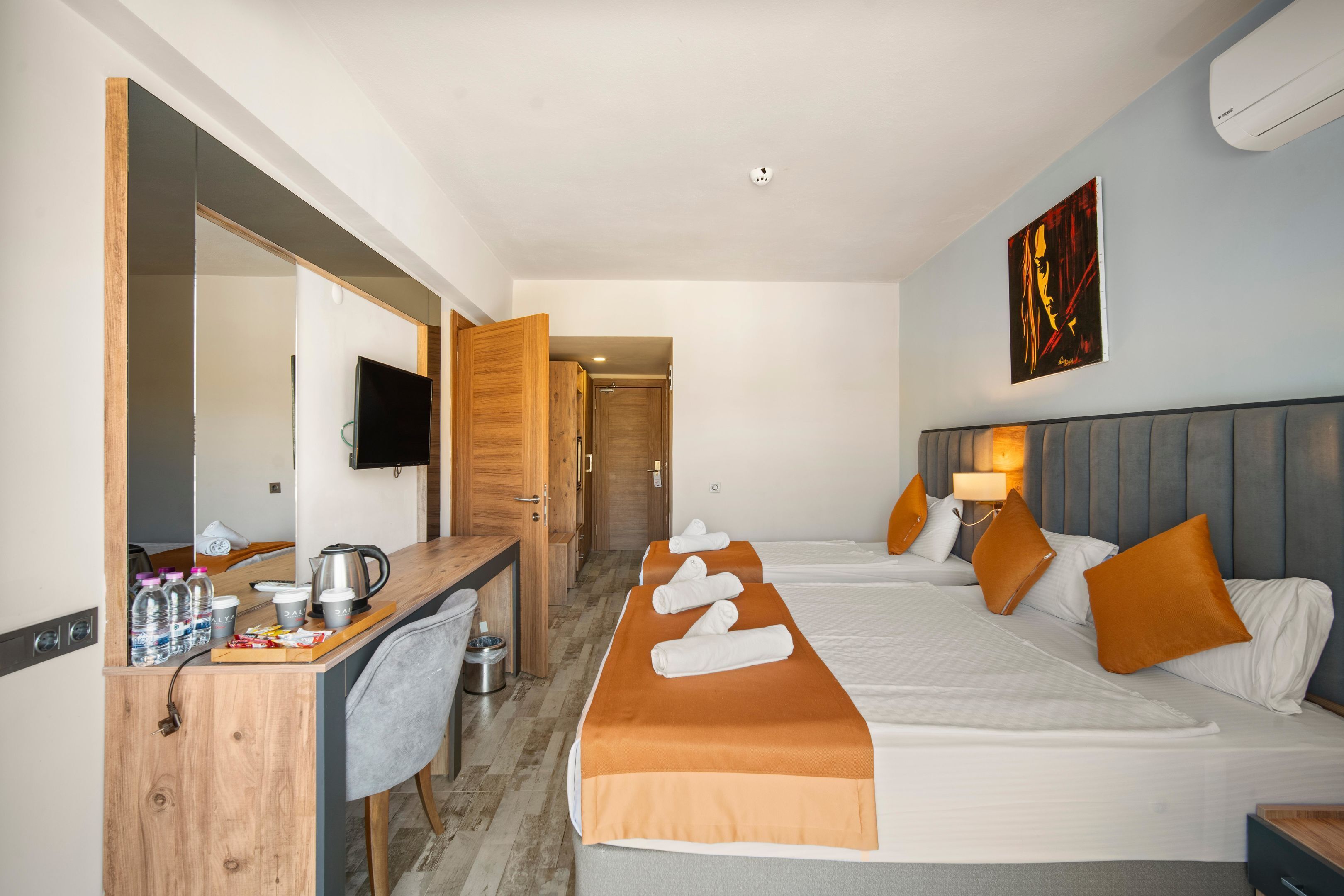 Une chambre d’hôtel avec un bureau, deux lits, une télévision et un tableau au mur.