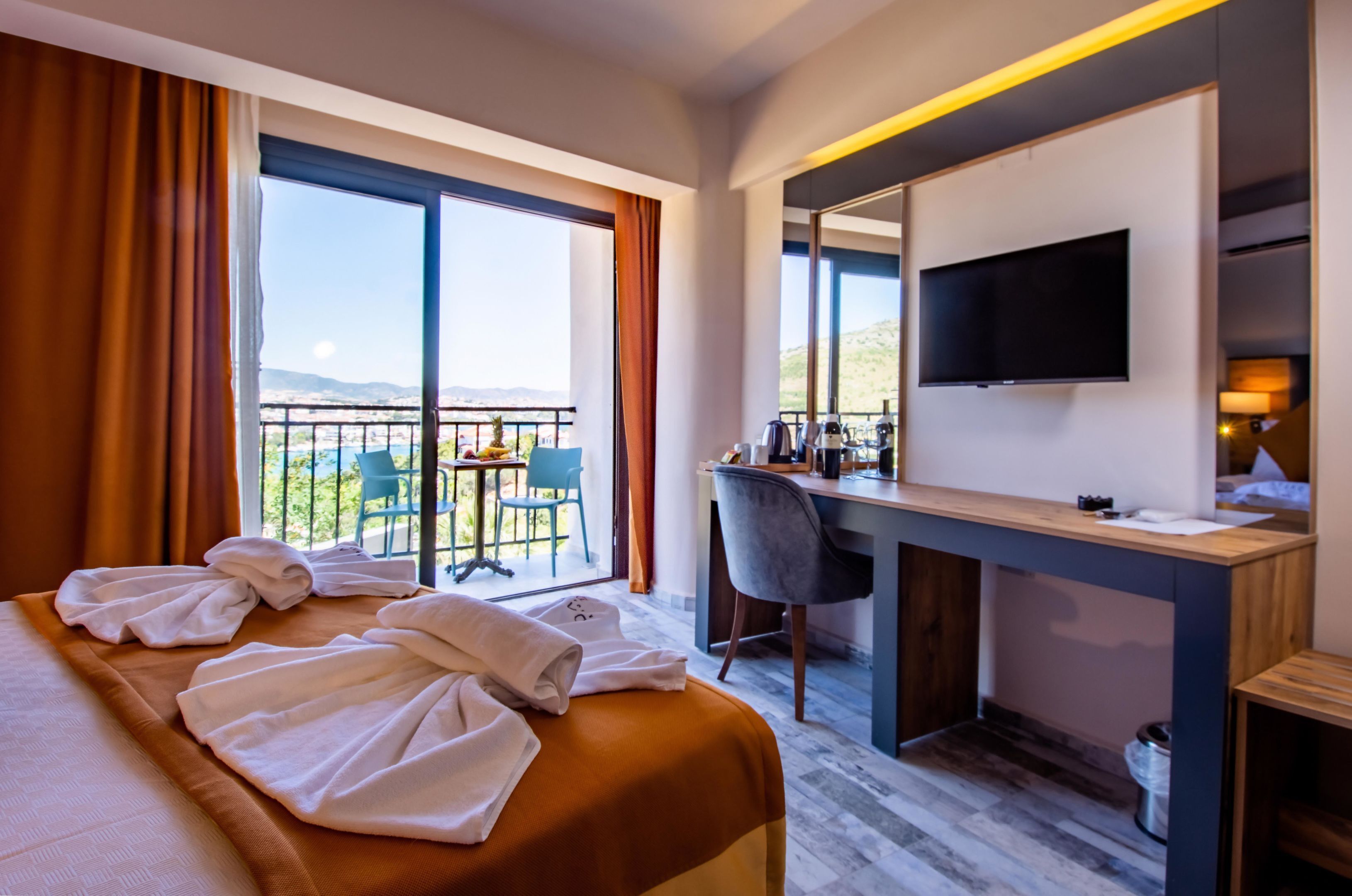 Habitación de hotel con cama, escritorio, silla, televisor y balcón con vistas a las montañas.