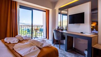 Habitación de hotel con cama, escritorio, silla, televisor y balcón con vistas a las montañas.